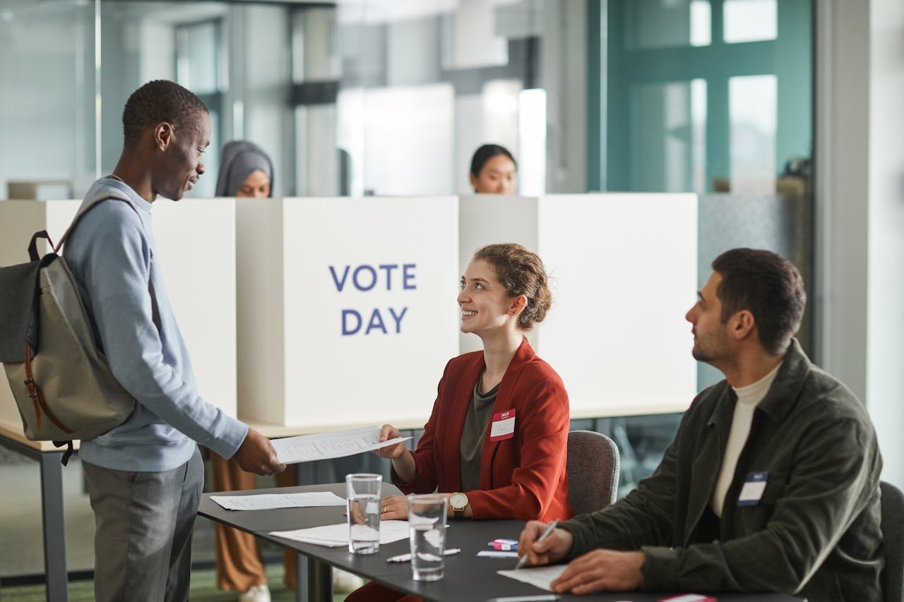 Diverse group of voters and officials at an indoor polling station on voting day.